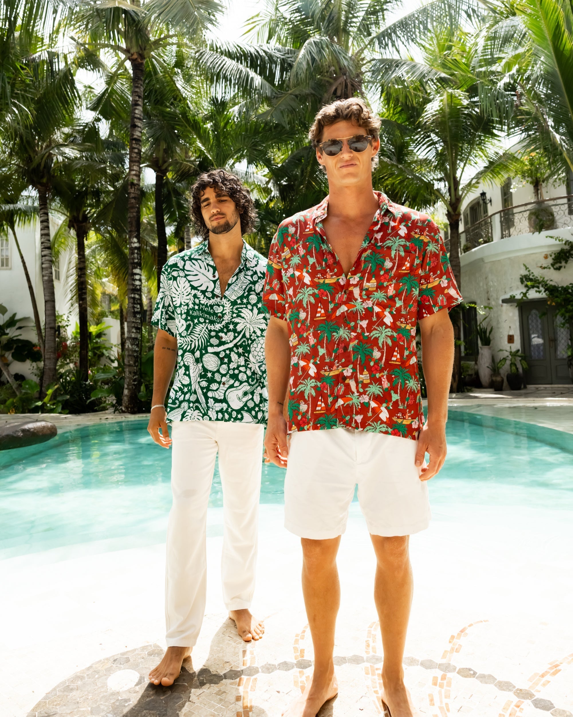 Two cool guys standing by a pool in christmas hawaiian shirts with palm trees in the background